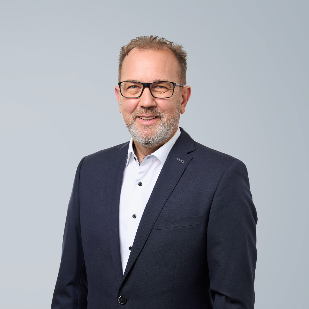 Porträt eines mittelalterlichen Geschäftsmannes mit Brille, in dunklem Anzug und weißem Hemd, vor einem neutralen grauen Hintergrund.