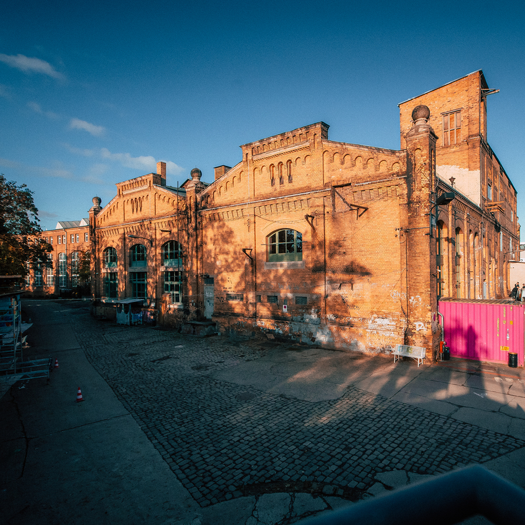 Ein altes, aus Ziegeln gebautes Industriegebäude bei Sonnenuntergang, dessen Fassade teilweise renoviert wird, gezeigt in warmen Farbtönen.