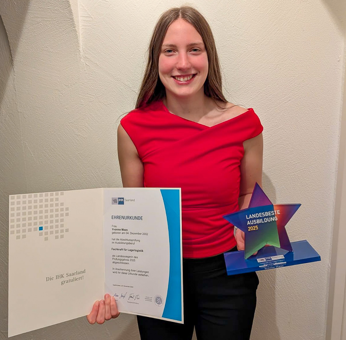 Junge Frau in rotem Oberteil hält stolz eine Ehrenurkunde und einen Auszeichnungstrophäe.