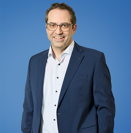 Porträt von Dr. Volker Baetz in Anzug vor blauem Hintergrund.