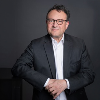 Porträt eines Mannes im Anzug, der lächelt und die Arme verschränkt.