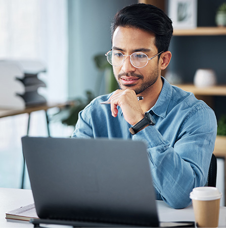 Ein Mann mit Brille arbeitet konzentriert an einem Laptop in einem modernen Büro.