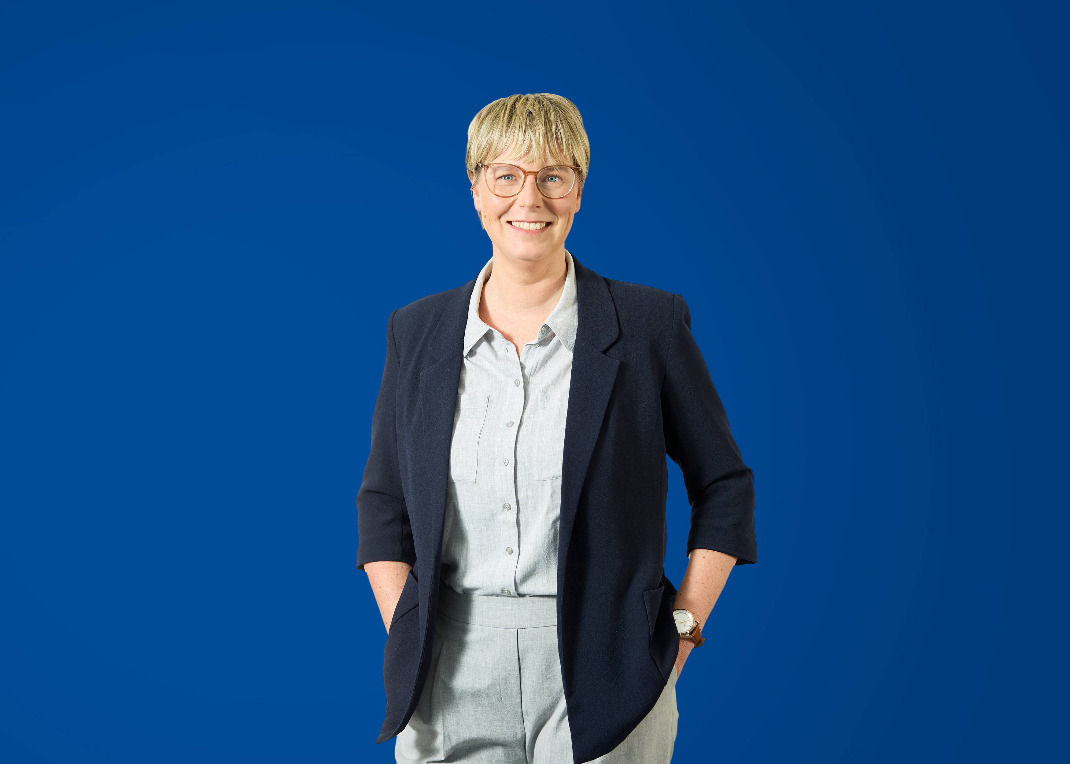 Professionelle Beratung für Energieversorger Person in formeller Kleidung mit blauer Wand im Hintergrund, lächelnd.