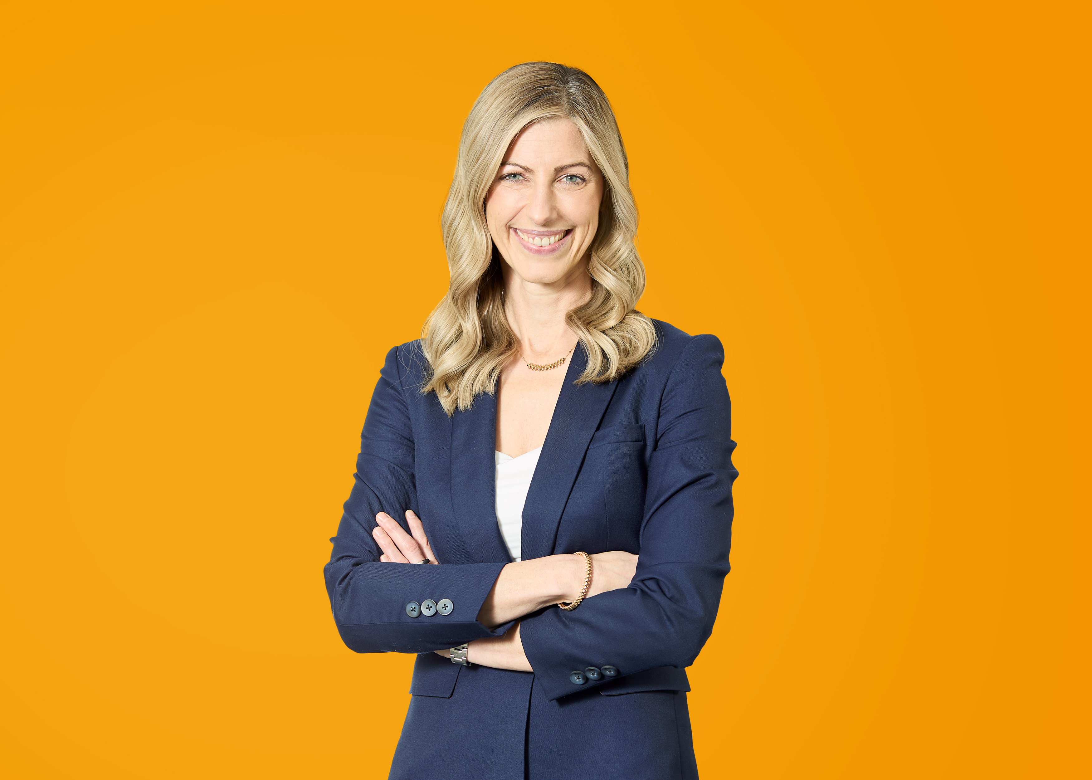 Professionelle Beratung für Energieversorger Frau in blauer Blazerjacke mit verschränkten Armen vor orangefarbenem Hintergrund.